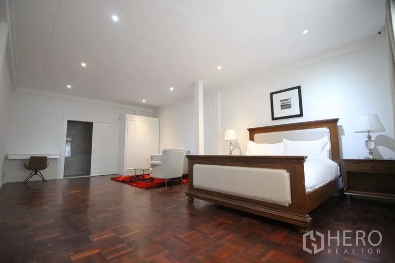 Detached House for rent in Chatuchak, Bangkok - Spacious master suite with dark parquet floors, classic wooden bed, seating area, desk, and door to ensuite.