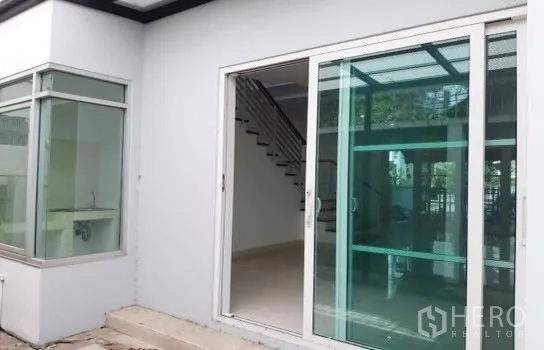 Home Office for rent in Wang Thonglang, Bangkok - Ground-floor entrance featuring large sliding glass doors, a corner window, and small exterior steps.