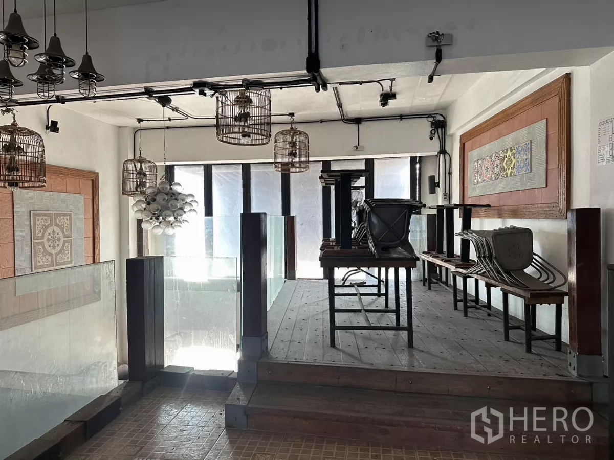 店屋 出租在Bang Na, Bangkok - 夹层就餐区，玻璃栏板、木平台与装饰性鸟笼吊灯。