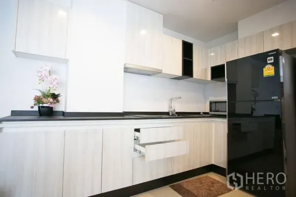 公寓 出租在Watthana, Bangkok - 现代L形厨房，白色橱柜与黑色台面，配大号冰箱。