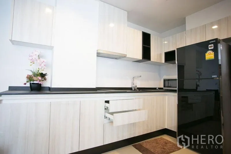 公寓 出租在Watthana, Bangkok - 现代L形厨房，白色橱柜与黑色台面，配大号冰箱。