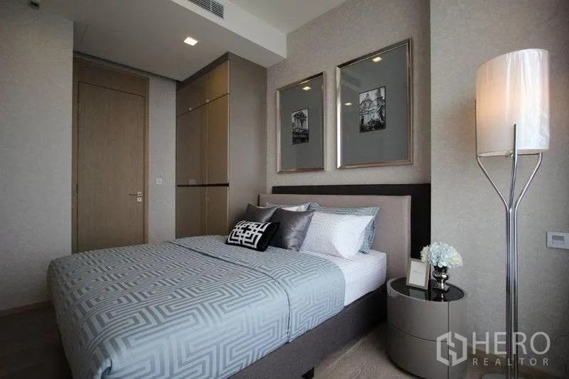 Condominium for rent in Watthana, Bangkok - Cozy bedroom with upholstered bed, framed artwork and tall floor lamp.