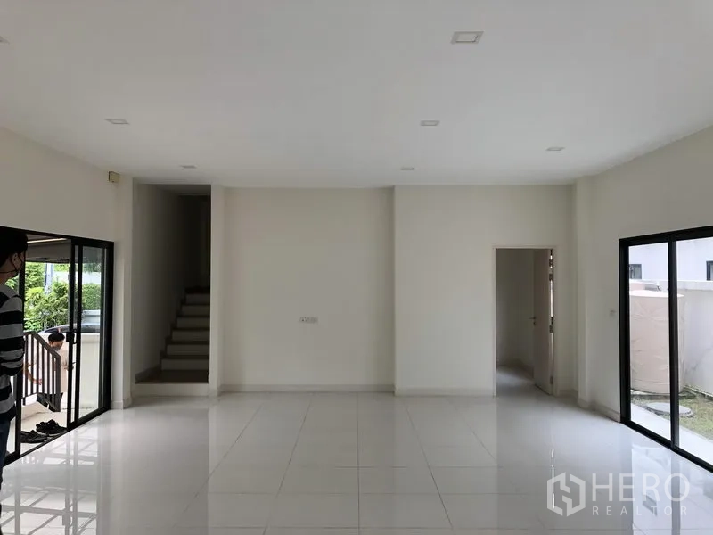 Townhouse for rent or sale in Saphan Sung, Bangkok - Large ground-floor living space with white tiles, stairway and multiple sliding doors.
