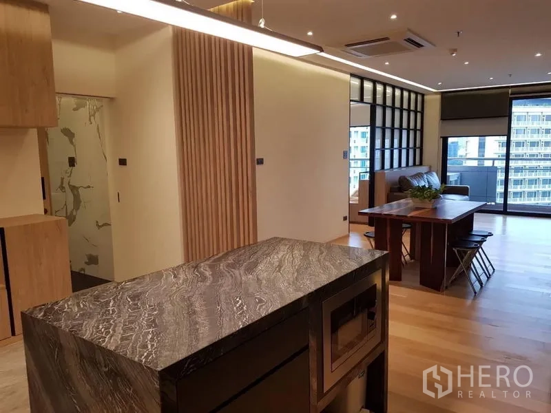 Condominium for rent in Bang Rak, Bangkok - View across the stone kitchen island to the living room with wood accents and balcony doors.