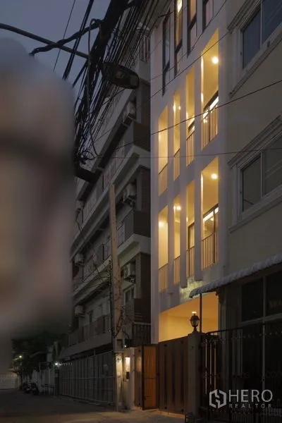 Townhouse for rent - Four-storey townhouse exterior with tall vertical windows illuminated at dusk on a quiet lane.