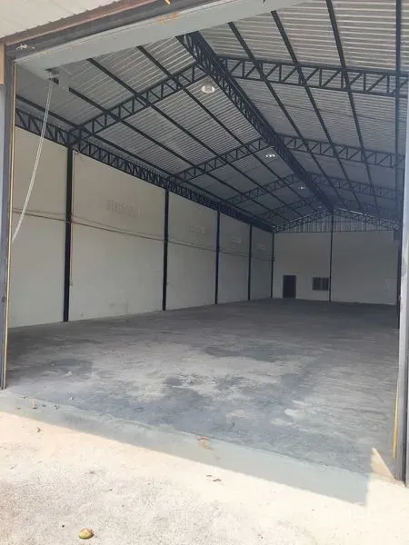 货栈 出租在Pathum Thani - 高挑钢桁架屋顶与混凝土地面的宽敞仓库内部，入口开阔。