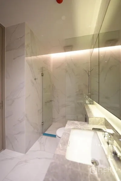 Condominium for rent - Marble bathroom with long vanity, backlit mirror and a glass walk-in shower.