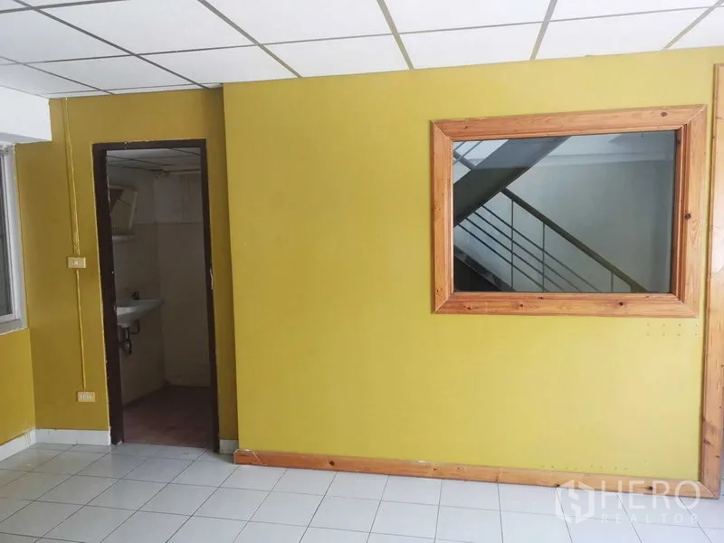 Factory for sale in Khlong Luang, Pathum Thani - Yellow-accent office with restroom access and wood-framed interior window.