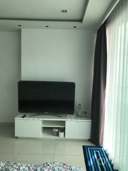 Condominium for rent in Bang Lamung, Chon Buri - Bright living area with large flat-screen TV on a white cabinet, glossy tile floors and full-height curtains.