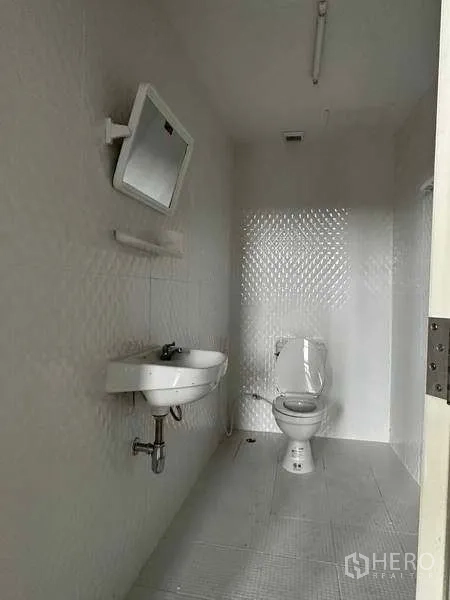 คลังสินค้า ให้เช่าในSamut Prakan - ห้องน้ำเรียบง่ายพร้อมโถสุขภัณฑ์ อ่างล้างหน้า กระจก และผนังปูกระเบื้องสีขาว