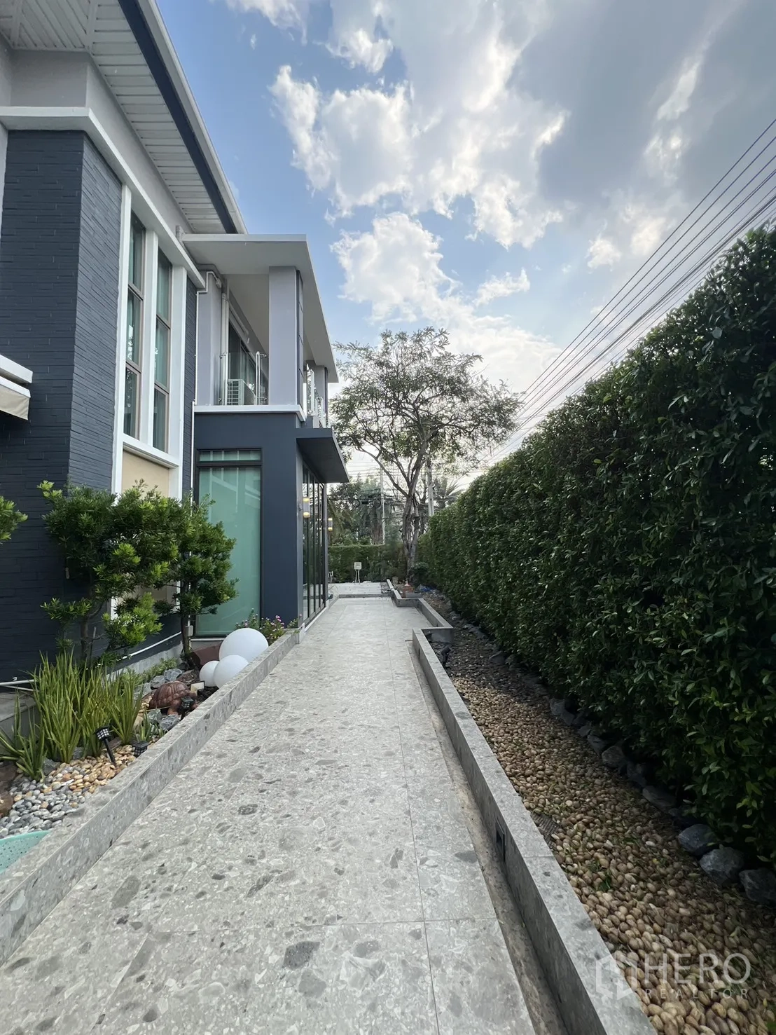 独栋房屋 for rent in Prawet, Bangkok - 现代两层独栋别墅侧边步道，绿篱成排，天空晴朗。