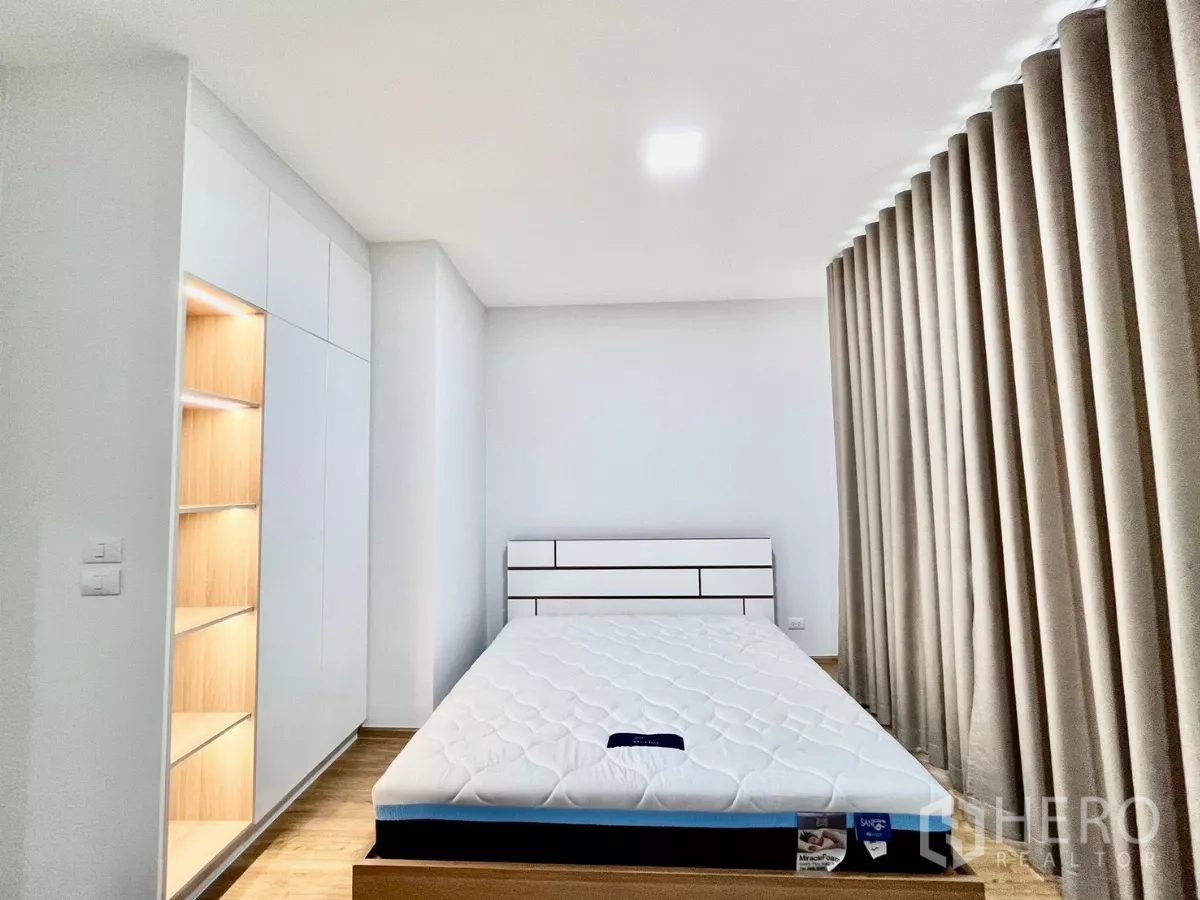Townhouse for rent in Bang Phli, Samut Prakan - Master bedroom with floor-to-ceiling curtains, built-in wardrobe, and illuminated shelving.