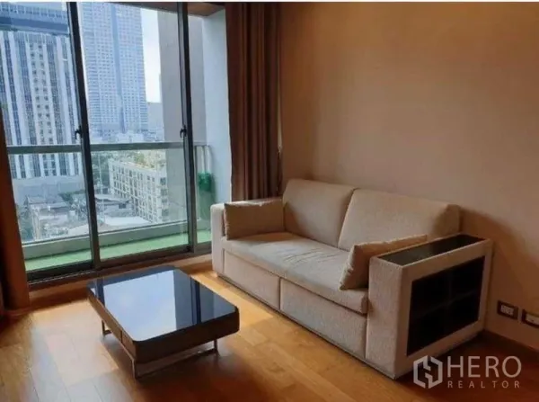 Condominium for rent in Bang Rak, Bangkok - Bright living room with beige sofa, glass coffee table and sliding doors to a balcony with Sathorn city skyline.