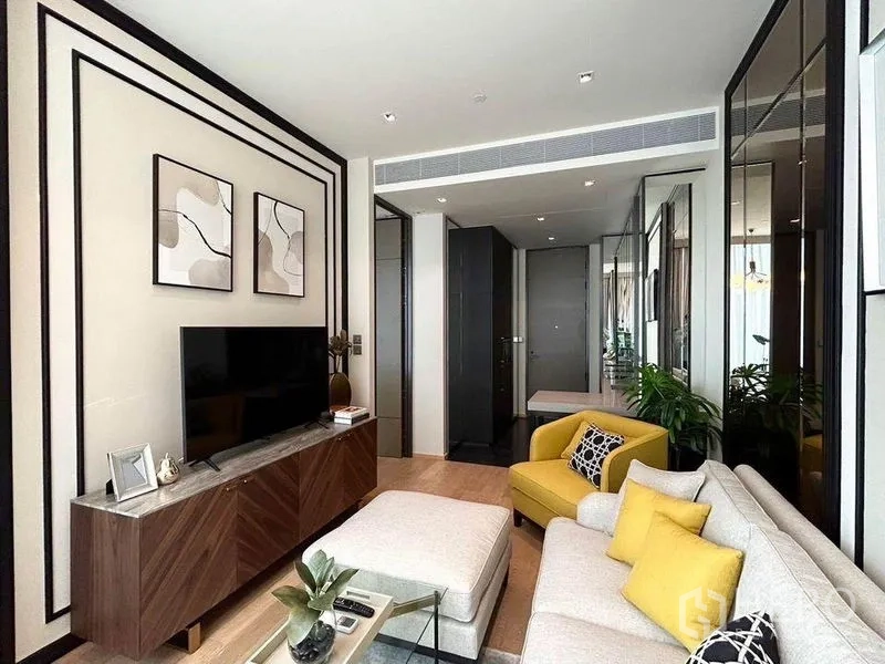 Condominium for rent in Pathum Wan, Bangkok - Living room with neutral sofa, ottoman, yellow chair and ceiling AC vent.