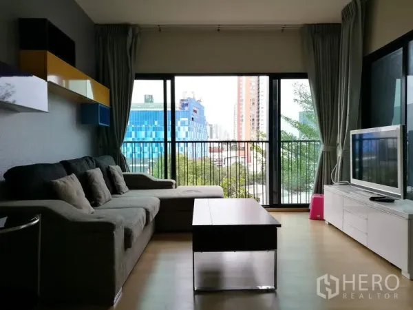 Condominium for rent in Watthana, Bangkok - Alternate view of the living area showing wall shelves, floor-to-ceiling glass and urban outlook from the balcony.