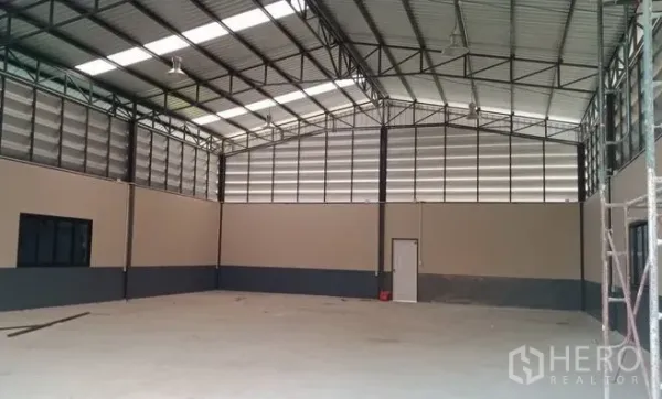 货栈 出售在Pathum Thani - 空置库房一角，钢结构屋架、通风百叶墙与侧门清晰可见。