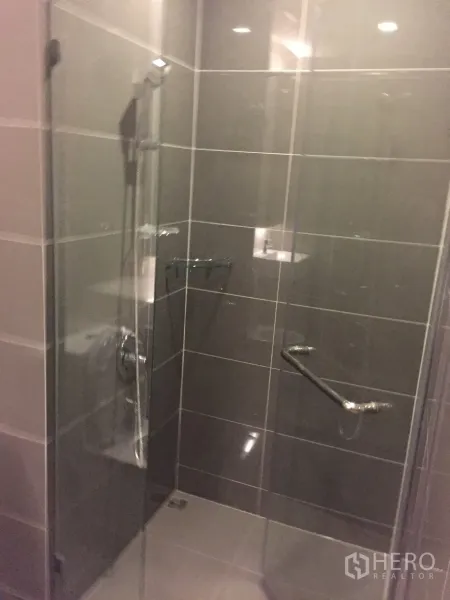 Condominium for rent in Watthana, Bangkok - Modern bathroom with glass-enclosed shower and gray tiled walls.