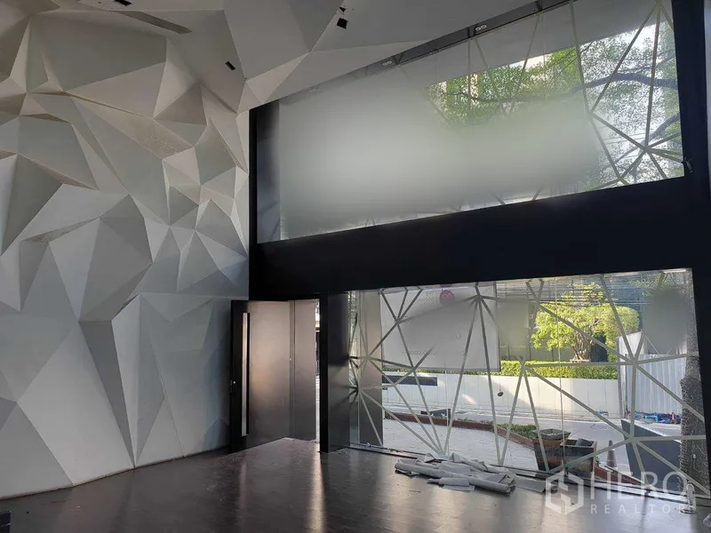 零售空间 出租在Khlong Toei, Bangkok - 挑高大堂，几何造型特色墙与双层落地窗，深色木地板。
