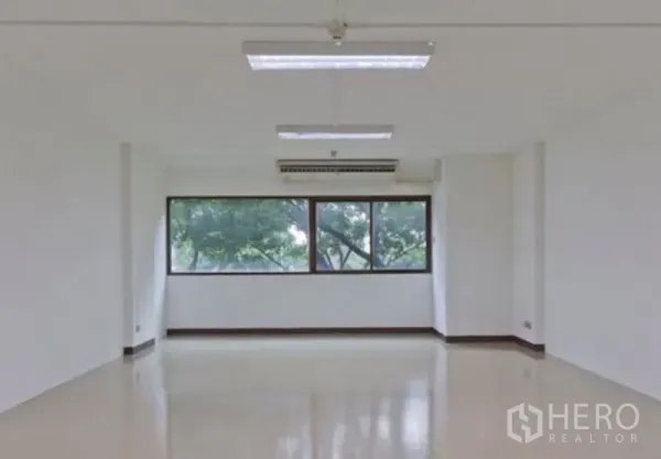 办公空间 出租在Chatuchak, Bangkok - 明亮空置办公室，大窗户可见绿树，天花板荧光灯与壁挂空调。