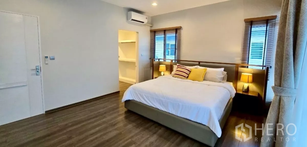 Detached House for rent in Samut Prakan - Master bedroom angle showing walk-in closet entry and wood-look floors.