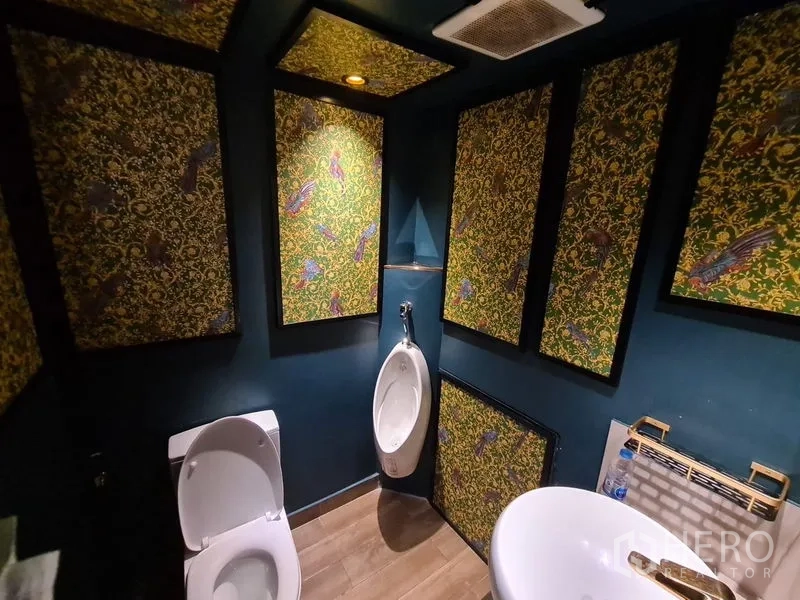 零售空间 出租在Bang Rak, Bangkok - 卫生间设装饰面板、坐便与小便器，暖光照明。