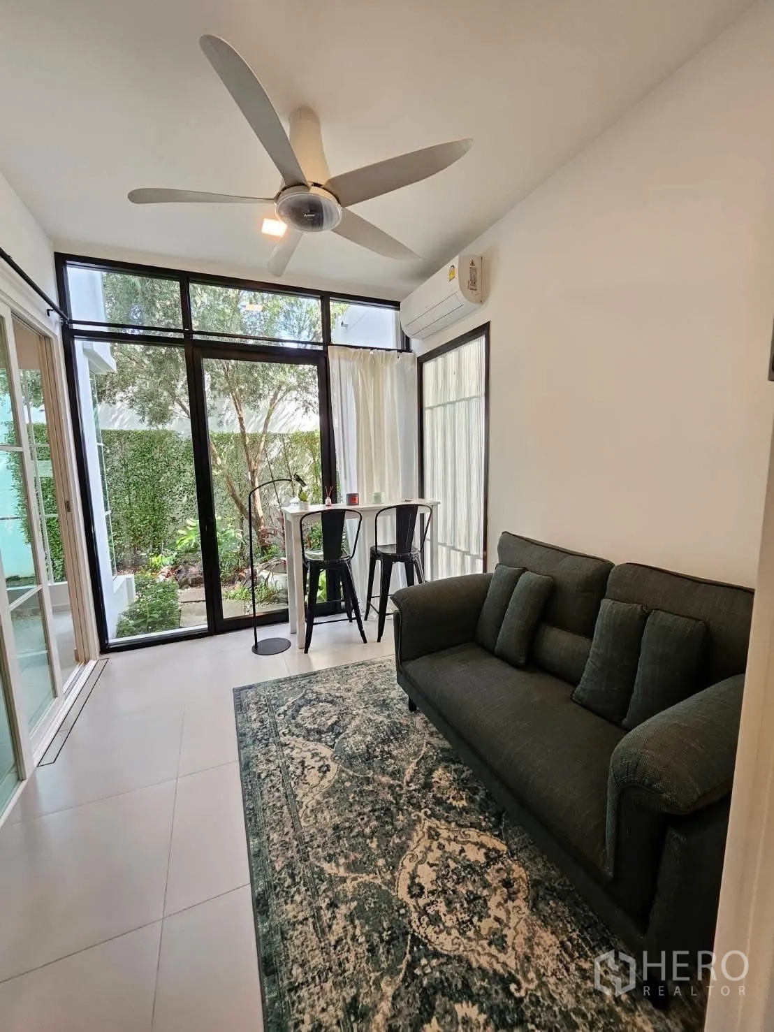 บ้านเดี่ยว for rent in Bang Phli, Samut Prakan - ซันรูมกระจกมีพัดลมเพดาน โซฟา โต๊ะบาร์และสตูล มองเห็นสวนสีเขียวด้านนอก