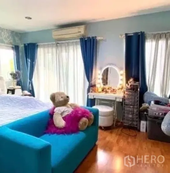 Detached House for sale in Khan Na Yao, Bangkok - Bright master bedroom with blue sofa, vanity table, wood flooring, and large windows with blue curtains.