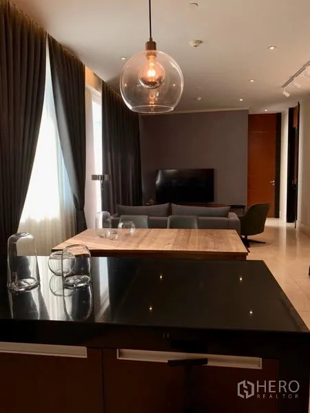 Condominium for rent in Bang Rak, Bangkok - View from the kitchen island toward the dining table and lounge with TV and draped curtains.