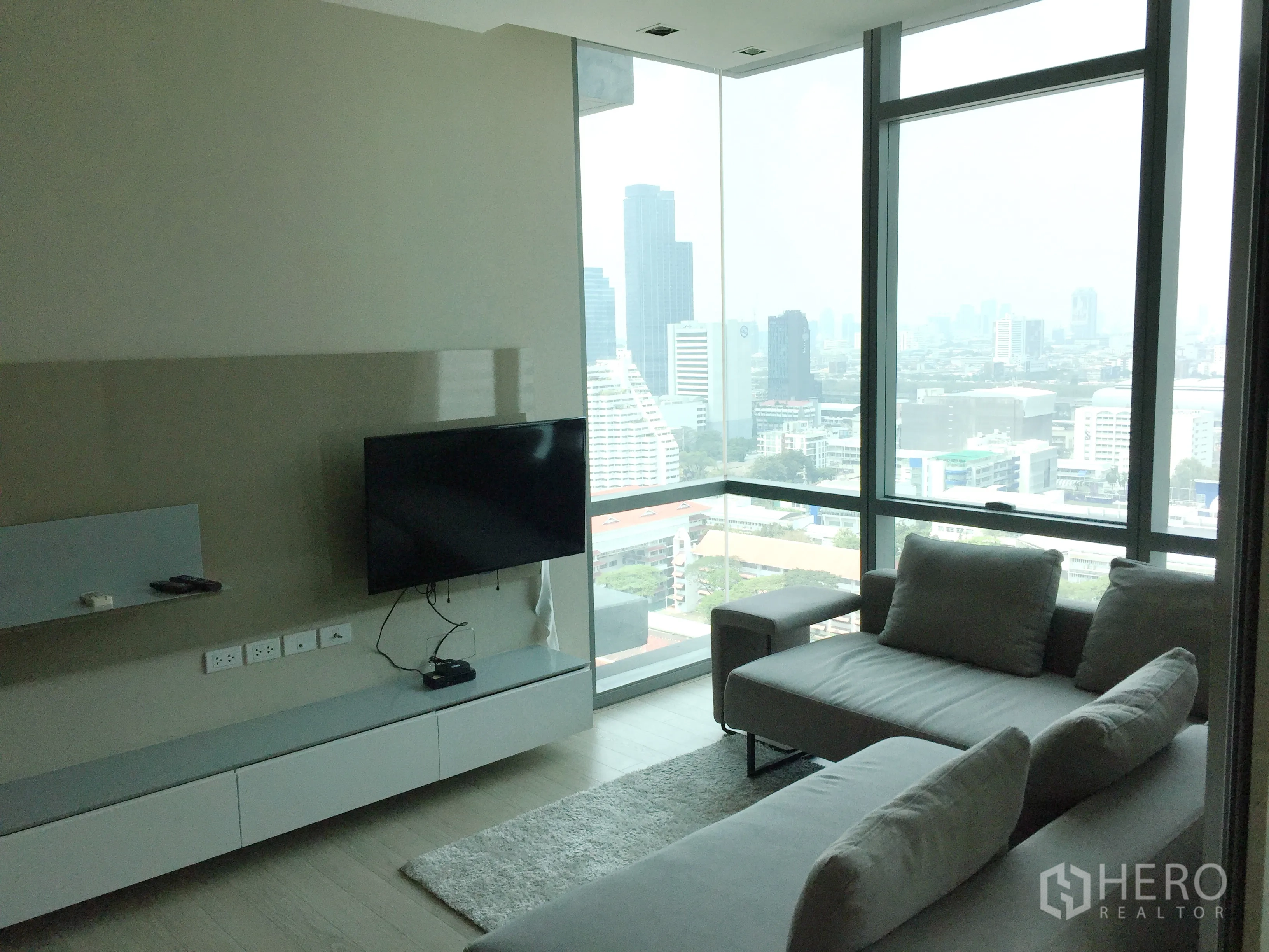 公寓 出租或出售在Watthana, Bangkok - 客厅转角落地窗，城市景观，壁挂电视与灰色组合沙发。