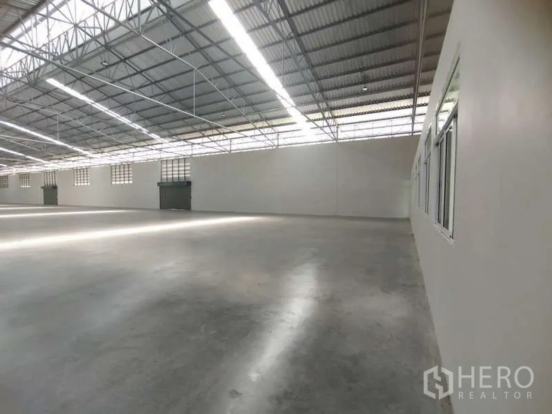 Warehouse for rent in Bang Pakong, Chachoengsao - Side view of the open warehouse floor with skylights, windows and roller shutter doors.