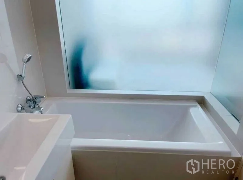Condominium for rent in Watthana, Bangkok - Bathroom with bathtub beside frosted glass window and hand shower.