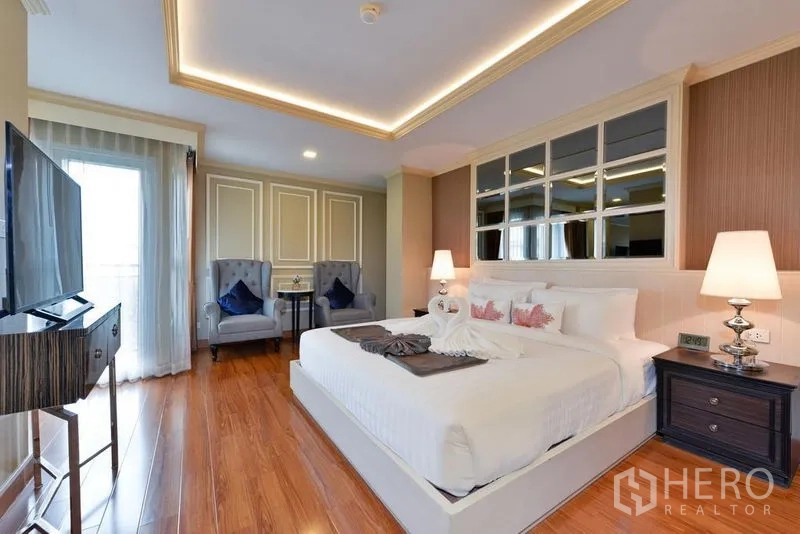 Apartment for rent in Khlong Toei, Bangkok - Master bedroom with king bed, feature wall, TV and sitting area by the balcony.