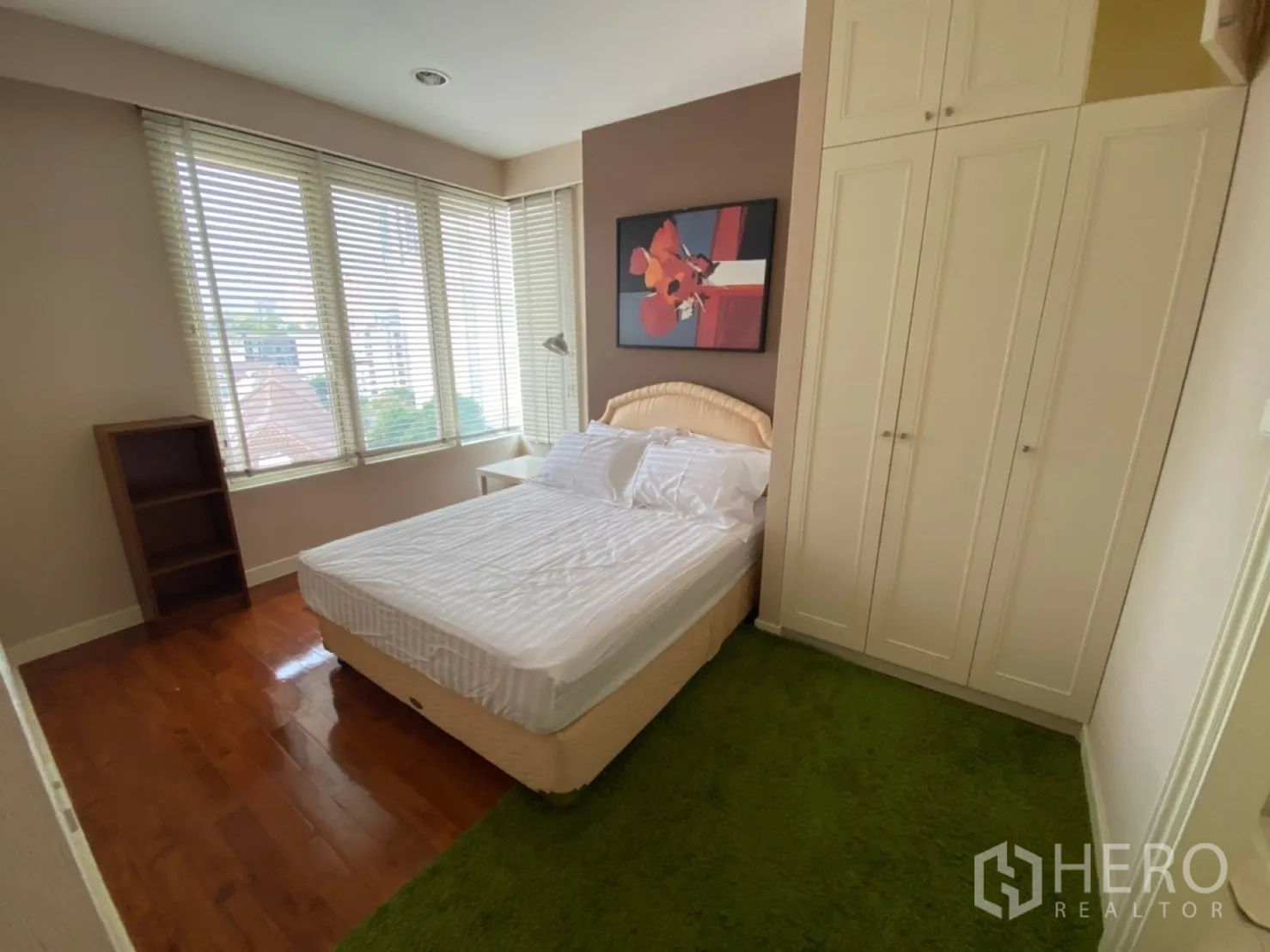 Condominium for rent in Watthana, Bangkok - Corner bedroom with double bed, green rug and wraparound windows.