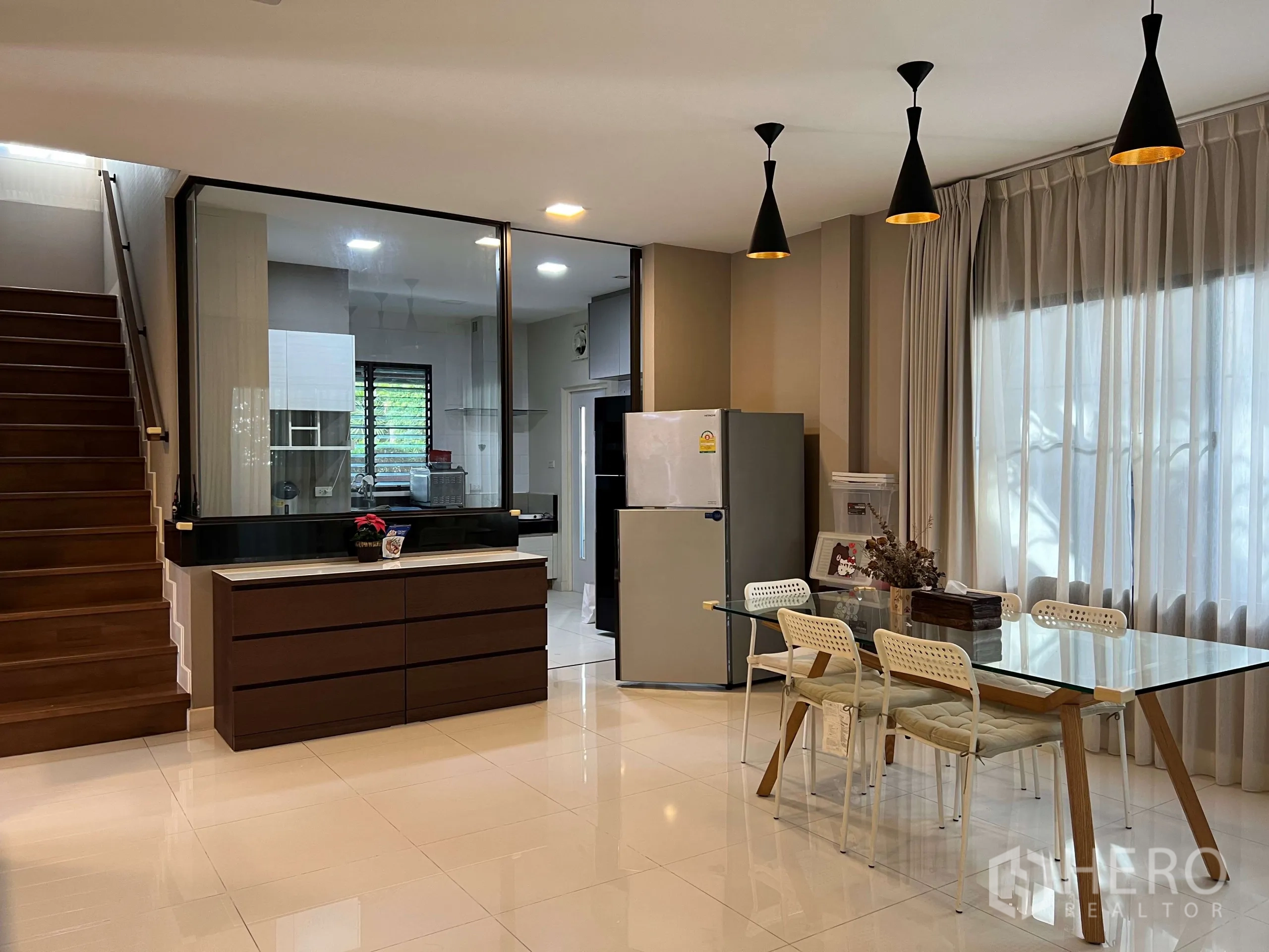 Detached House for rent in Prawet, Bangkok - Dining area with glass table, pendant lights and stairs beside floor-to-ceiling curtains.
