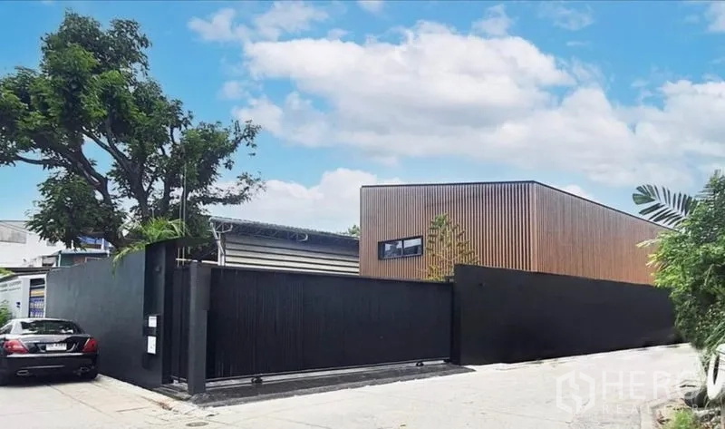 Home Office for rent or sale in Khlong Toei, Bangkok - Street view of a corner lot with a high black wall and a modern timber-clad building.