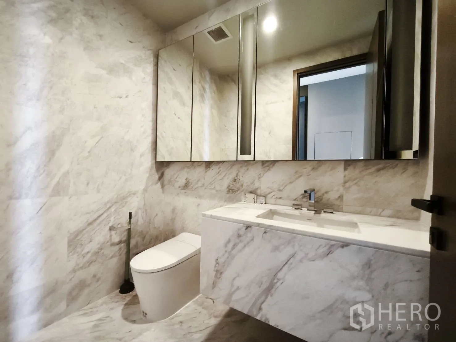 Condominium for rent in Watthana, Bangkok - Guest bathroom with marble walls, mirrored cabinets, and vanity.