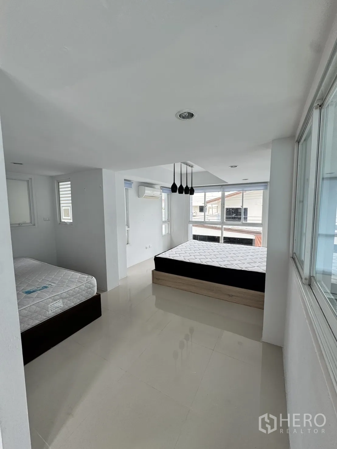 Home Office for rent in Watthana, Bangkok - Spacious bedroom with two platform beds, pendant lights, and corner windows.