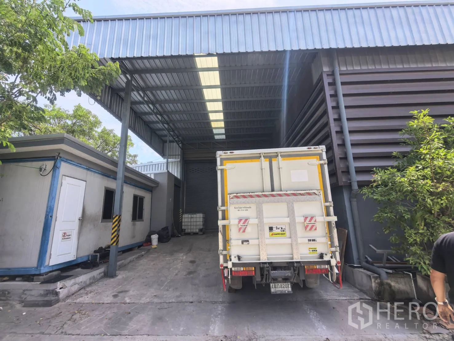 Warehouse for rent in Bang Sao Thong, Samut Prakan - Sheltered loading area with a truck beside a small site office and roller door.