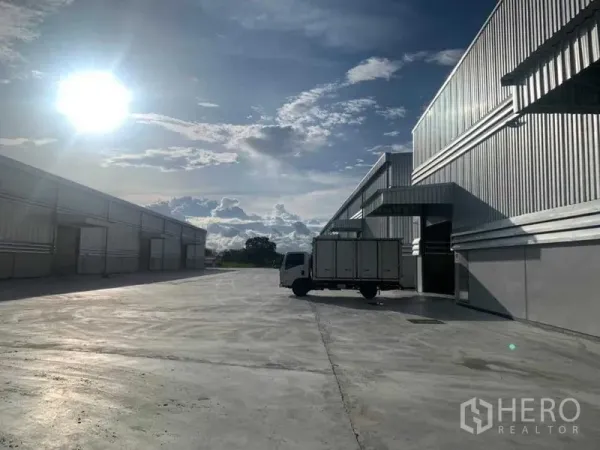 Warehouse for rent in Ban Bueng, Chon Buri - Truck positioned at a loading bay between warehouses with a broad concrete apron under afternoon sun.