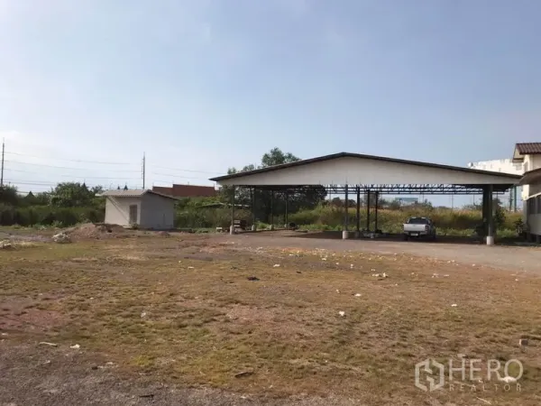 Land for sale in Mueang Samut Sakhon, Samut Sakhon - Vacant land with a small utility hut, green borders and a covered parking shed.