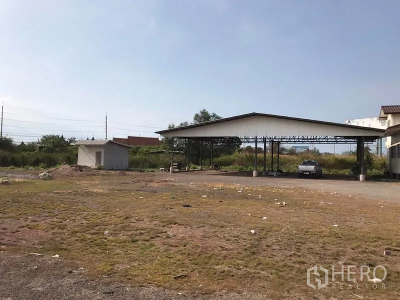 Land for sale in Mueang Samut Sakhon, Samut Sakhon - Vacant land with a small utility hut, green borders and a covered parking shed.