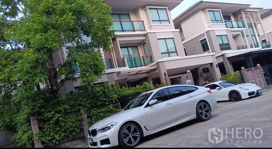 บ้าน ให้เช่าหรือขายในKhan Na Yao, Bangkok - ด้านหน้าแบบบ้านเดี่ยวสามชั้นสมัยใหม่ มีระเบียง โรงจอดรถ และต้นไม้ใหญ่