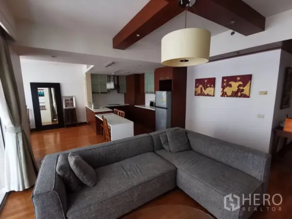 Condominium for rent in Pathum Wan, Bangkok - Open-plan living room with gray sectional, wood floors, and open kitchen in a Lumphini, Bangkok condo.