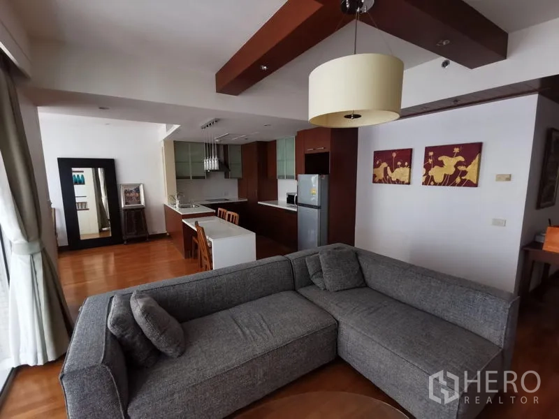 Condominium for rent in Pathum Wan, Bangkok - Open-plan living room with gray sectional, wood floors, and open kitchen in a Lumphini, Bangkok condo.