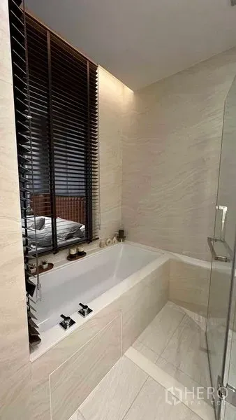 Condominium for sale - Deep soaking bathtub beside a window with blinds and stone‑look tiles.