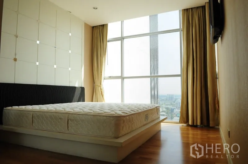 Condominium for rent in Pathum Wan, Bangkok - Sunlit bedroom with floor-to-ceiling windows, city view, curtains and warm wood flooring.
