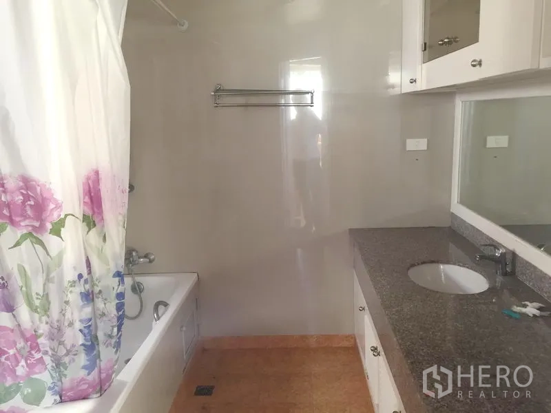 Condominium for rent in Watthana, Bangkok - Bathroom with bathtub, floral shower curtain, large mirror and granite-top vanity.