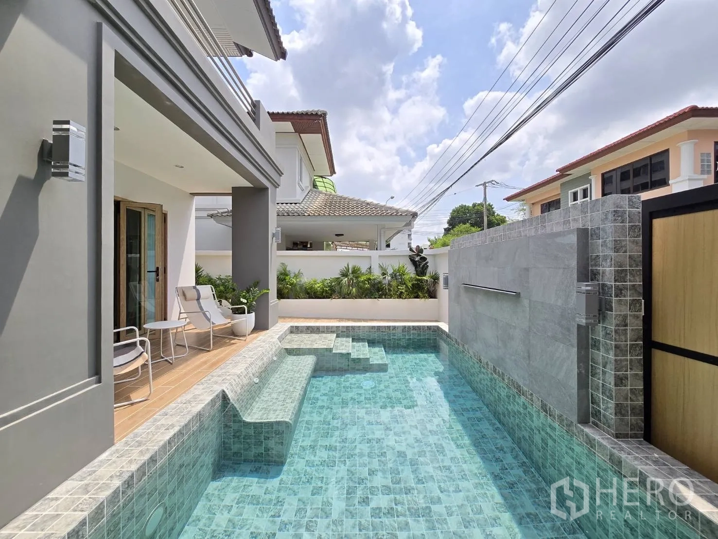 独立式住宅 出售在Suan Luang, Bangkok - 长条形泳池沿木质平台延伸，配高隐私围墙与绿植。