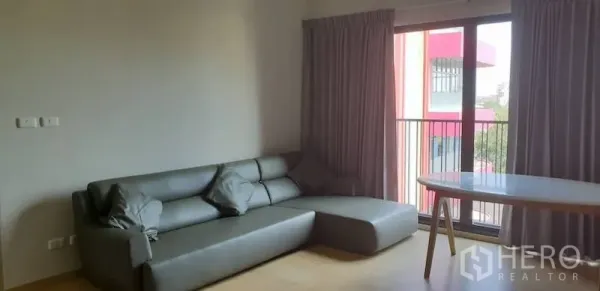 Condominium for rent in Watthana, Bangkok - Living room with a gray sectional sofa, round dining table and sliding doors opening to a balcony.