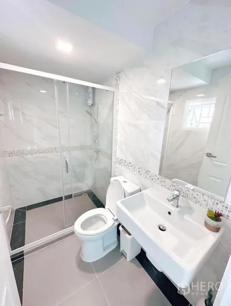 Detached House for rent in Bueng Kum, Bangkok - Contemporary bathroom with glass-enclosed shower, toilet, wide mirror and tiled walls.